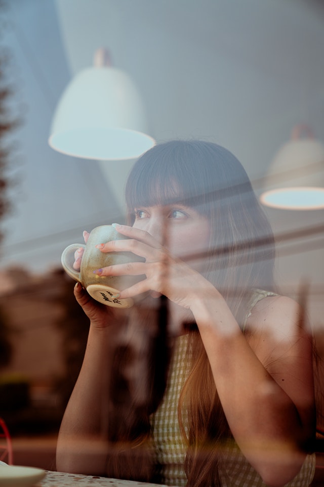 female looking out of window drinking a coffee